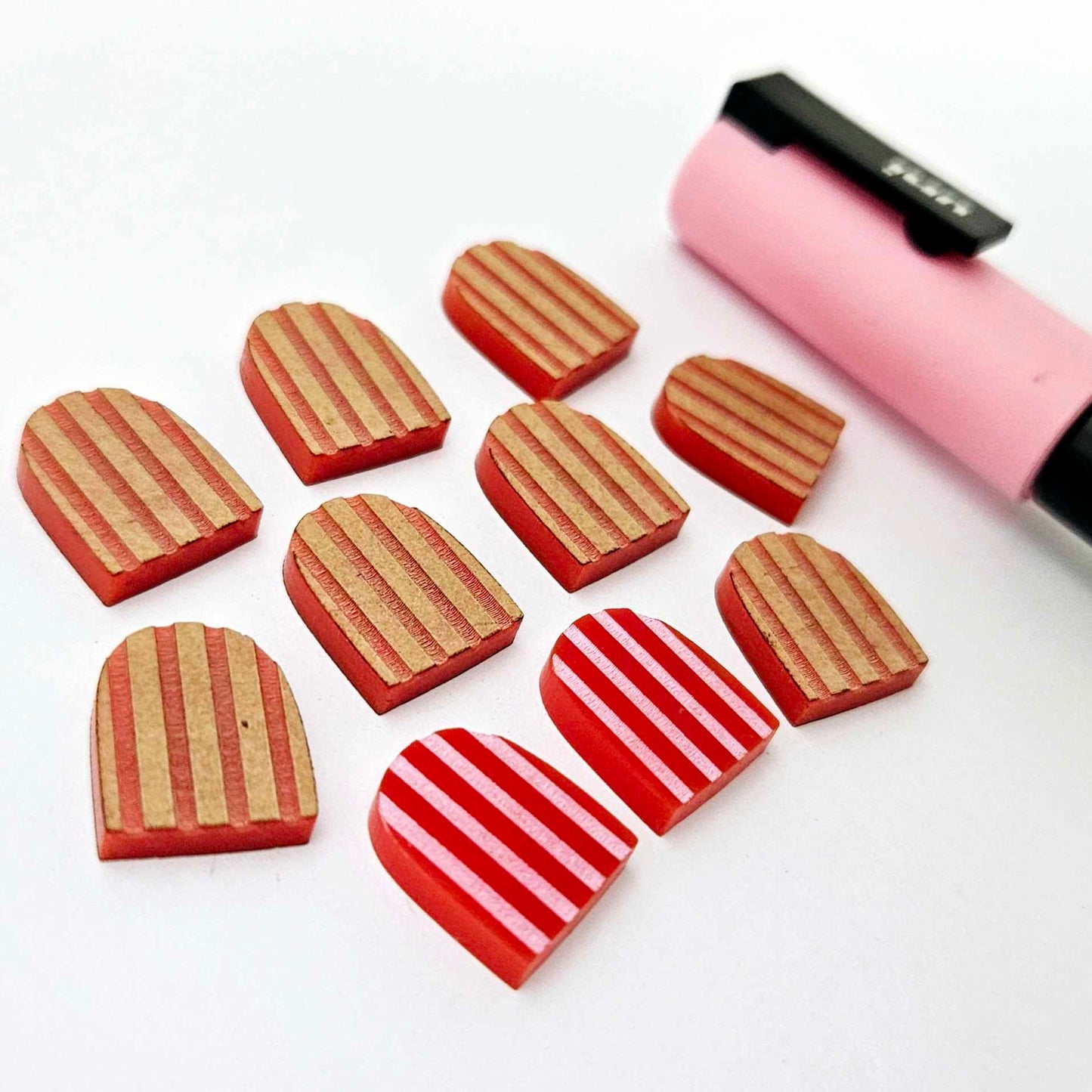 16mm red striped acrylic arch stud blanks showing paint filled example and unpainted pieces with protective film, pictured with a light pink Posca paint pen