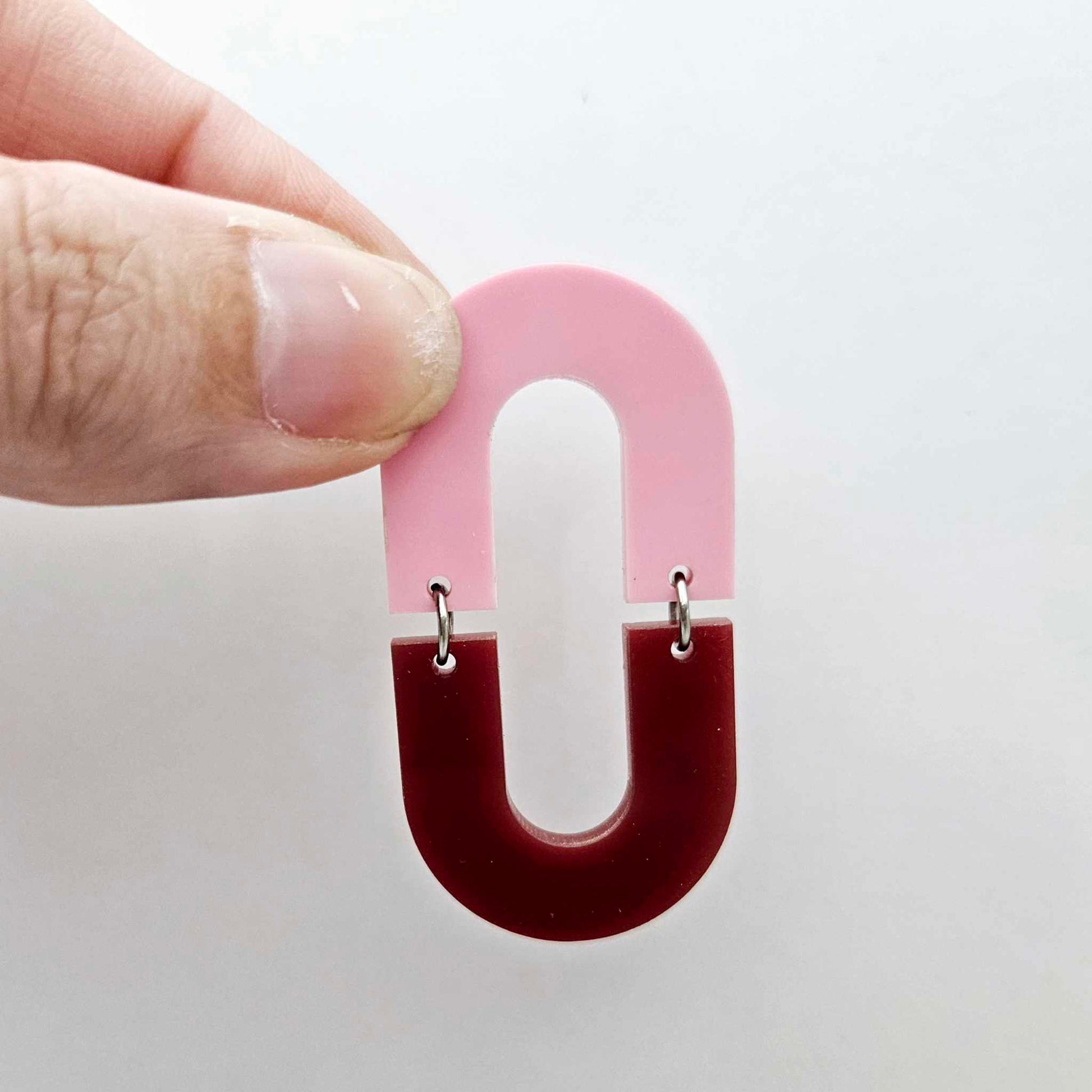 Layered U shape dangle earring in pastel pink and port wine (burgundy) acrylic, assembled into an open oval design hanging as a statement stud dangle