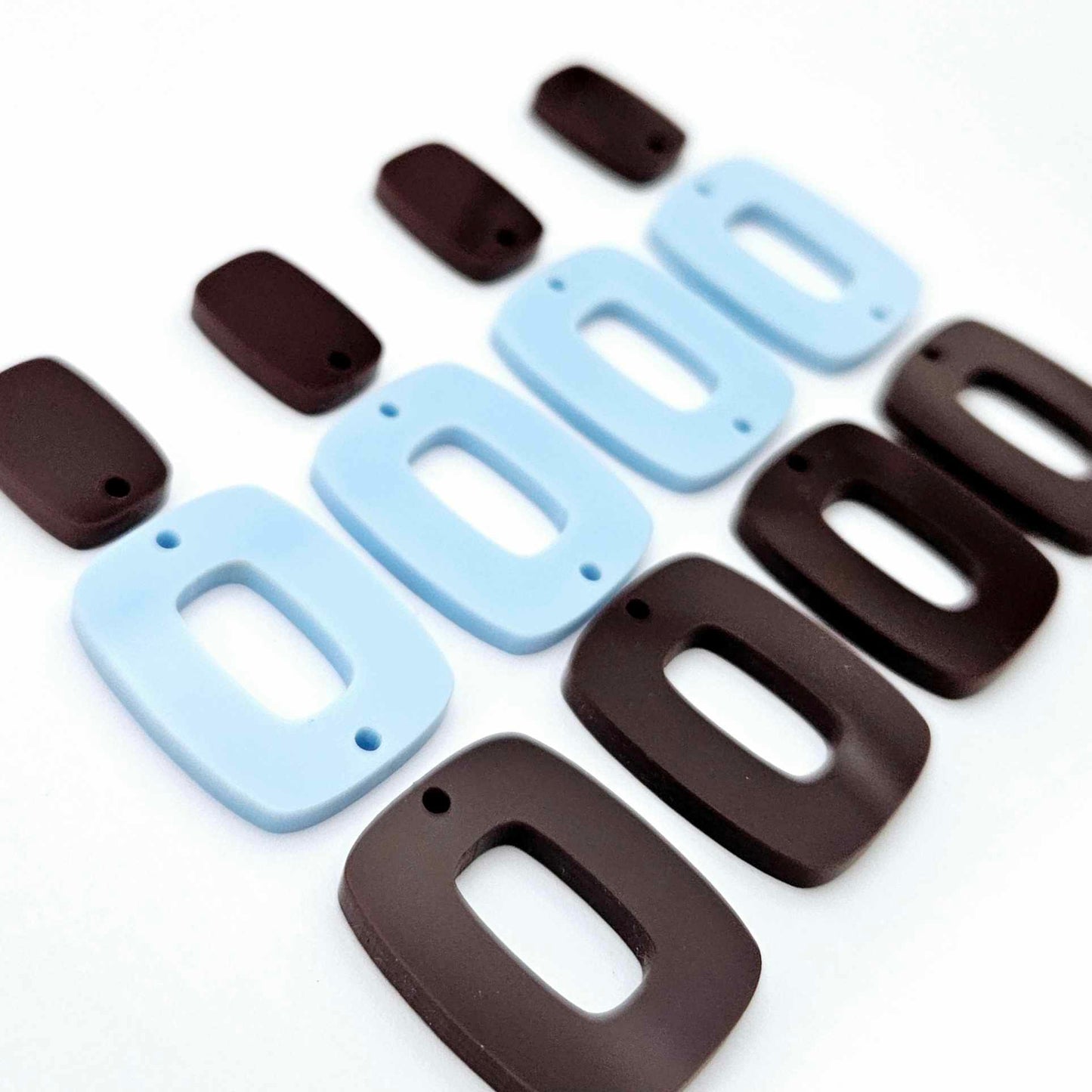 Two pairs of layered rectangle dangle blanks in chocolate brown and pastel blue acrylic, unassembled pieces laid flat showing three-piece design