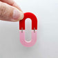 Layered U shape dangle earring in pastel pink and red acrylic, assembled into an open oval design hanging as a statement stud dangle