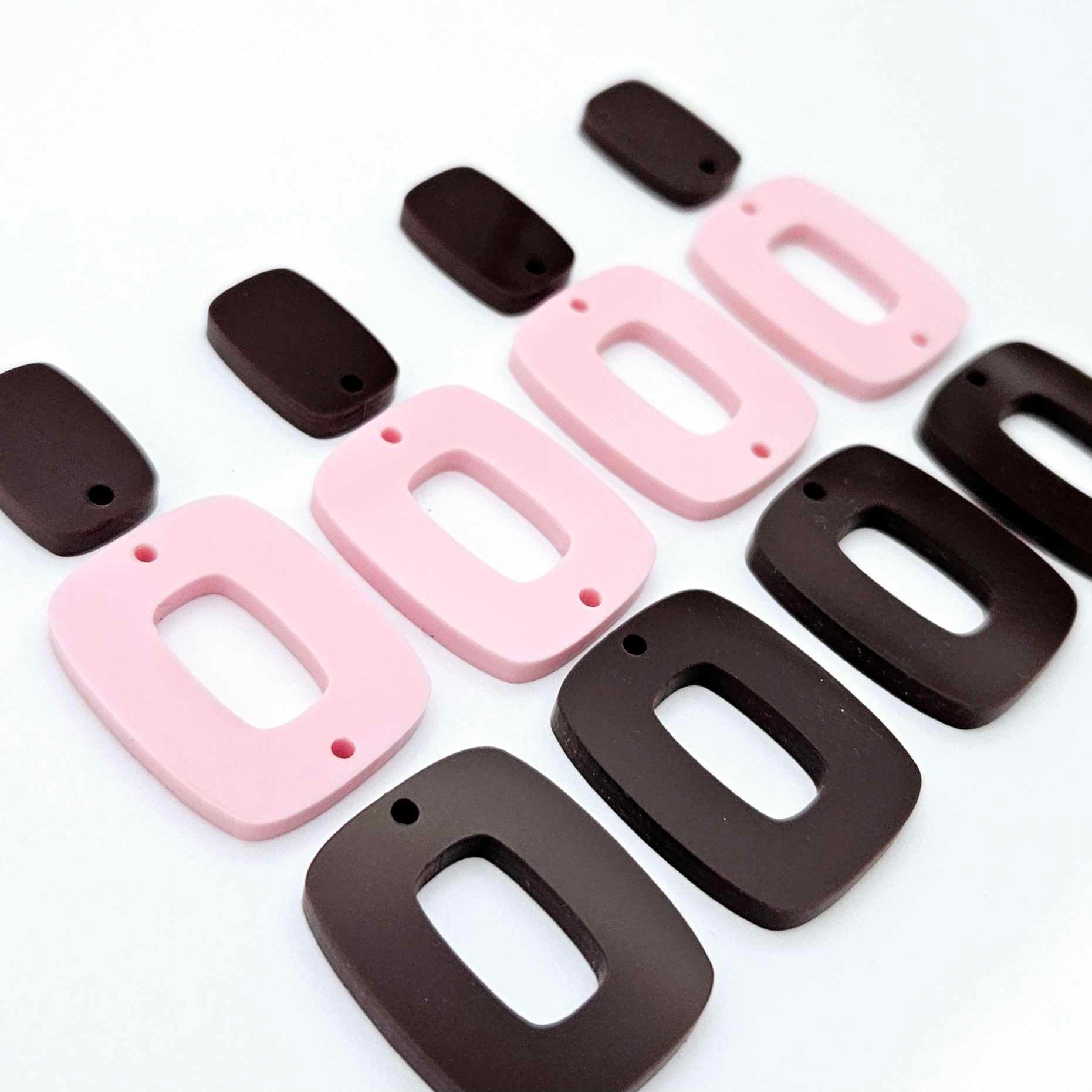 Two pairs of layered rectangle dangle blanks in chocolate brown and pastel pink acrylic, unassembled pieces laid flat showing three-piece design
