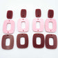 Two pairs of layered rectangle dangle blanks in port wine and pastel pink acrylic, unassembled pieces laid flat showing three-piece design