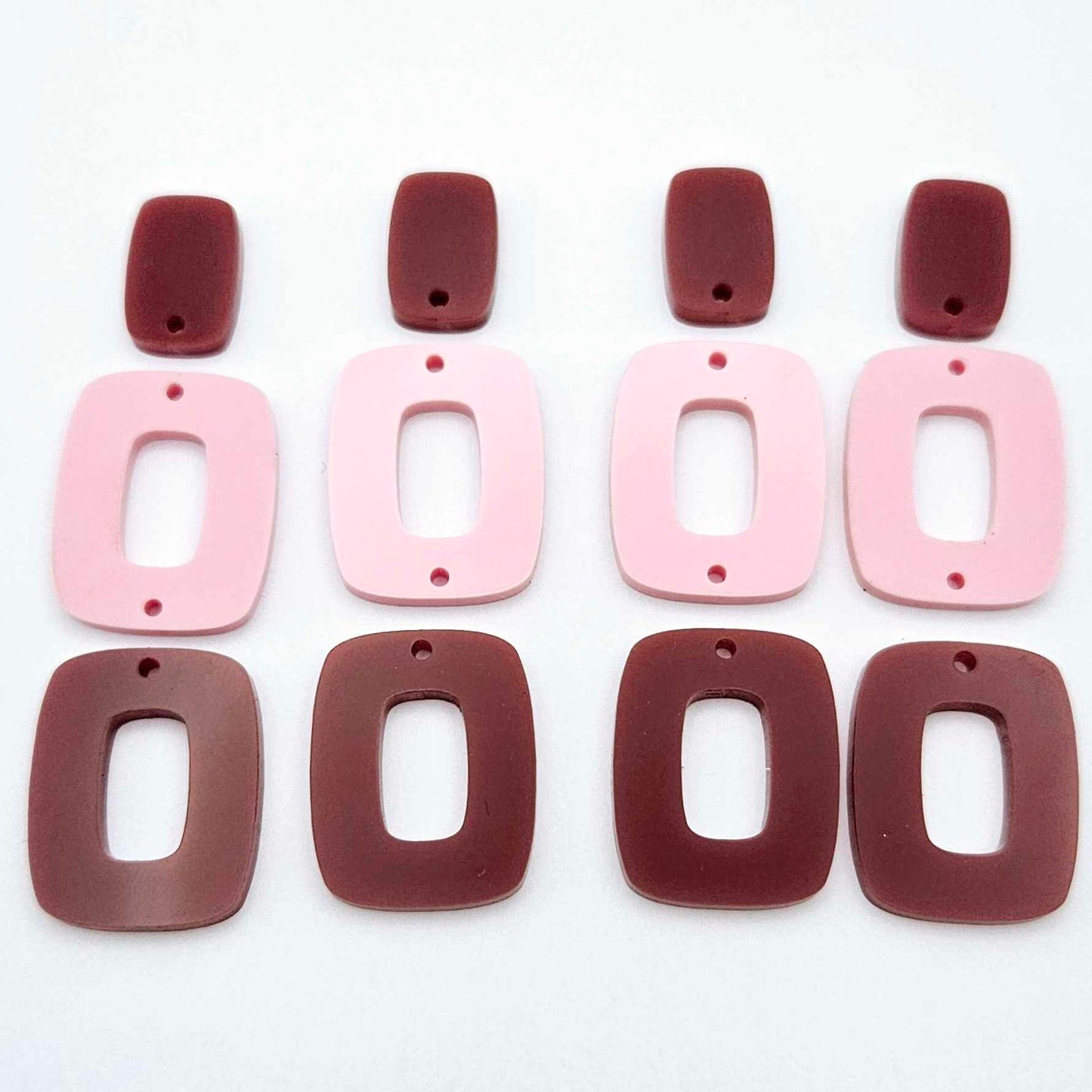 Two pairs of layered rectangle dangle blanks in port wine and pastel pink acrylic, unassembled pieces laid flat showing three-piece design