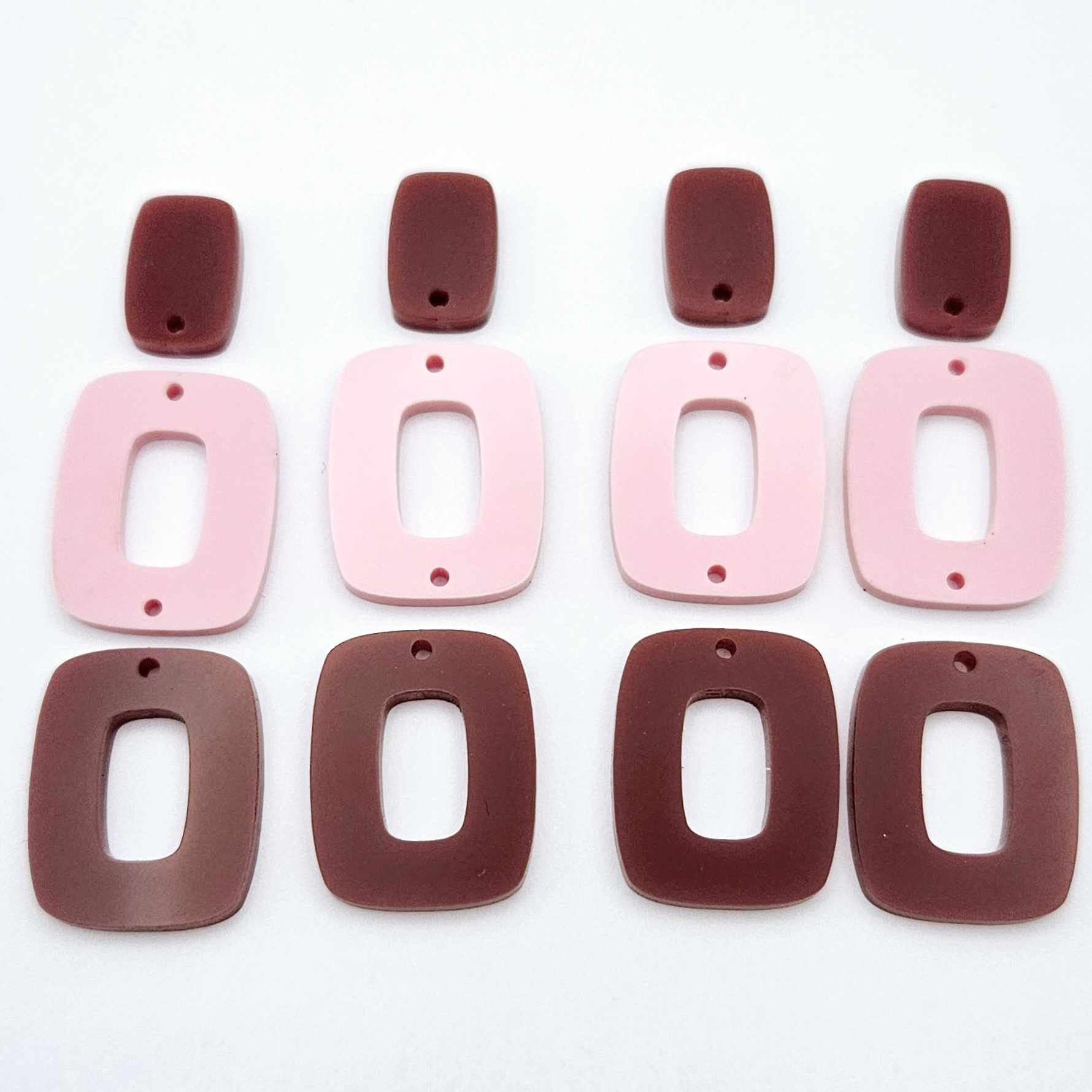 Two pairs of layered rectangle dangle blanks in port wine and pastel pink acrylic, unassembled pieces laid flat showing three-piece design