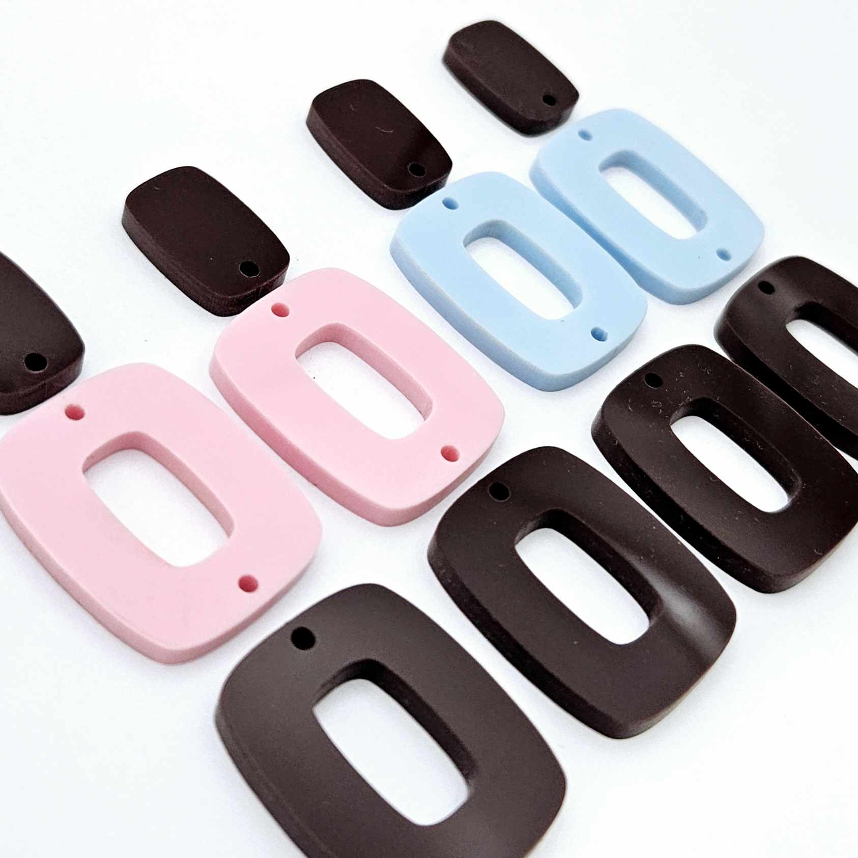 Two pairs of layered rectangle dangle blanks in chocolate brown and pastel pink/blue acrylic, unassembled pieces laid flat showing three-piece design