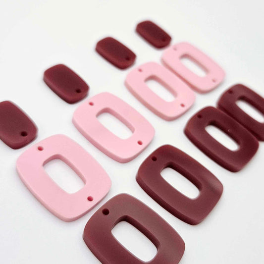 Two pairs of layered rectangle dangle blanks in port wine and pastel pink acrylic, unassembled pieces laid flat showing three-piece design
