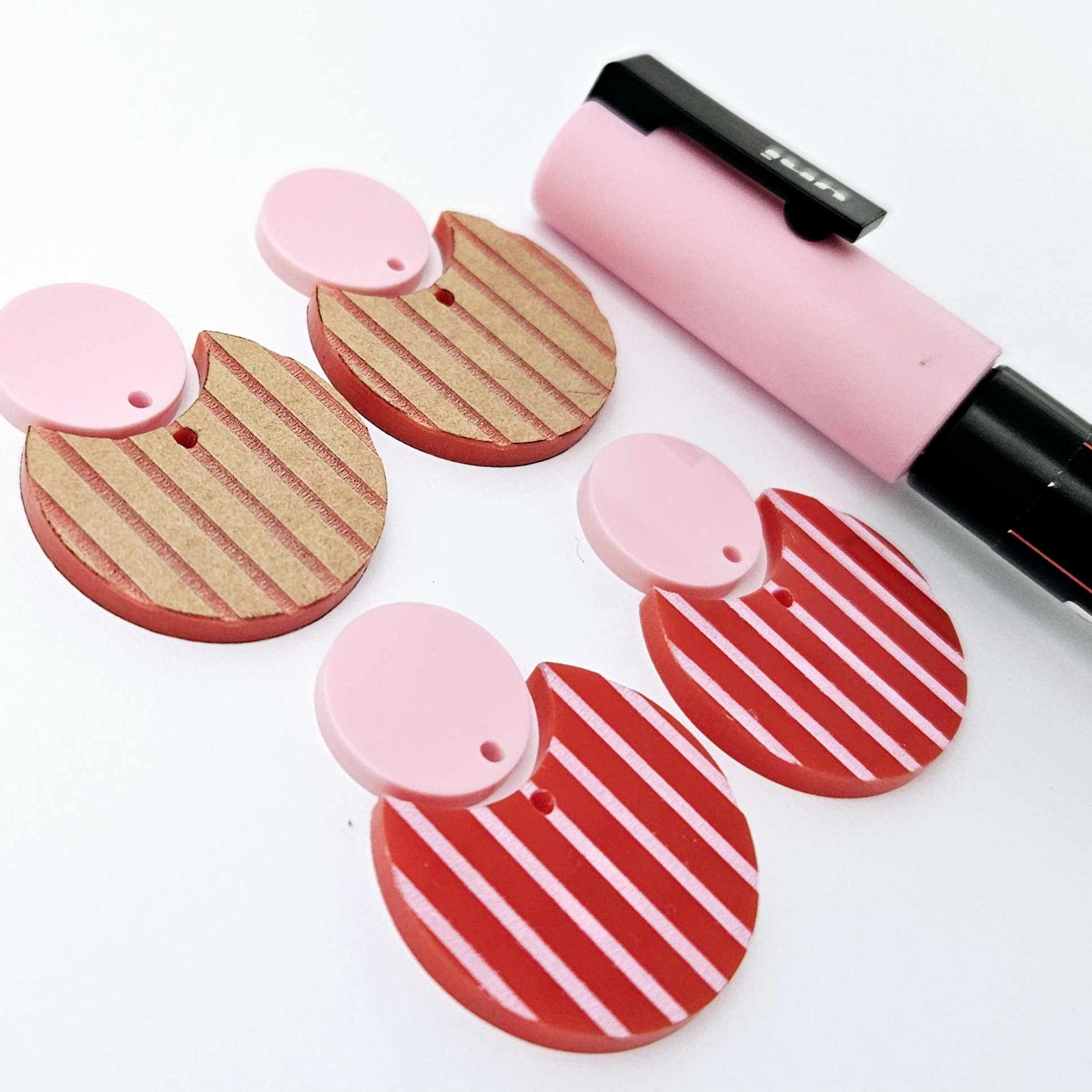 Nested circle dangle blanks showing one pair paint filled light pink and peeled, with another pair unpainted and with protective film on, pictured with a pink Posca paint pen