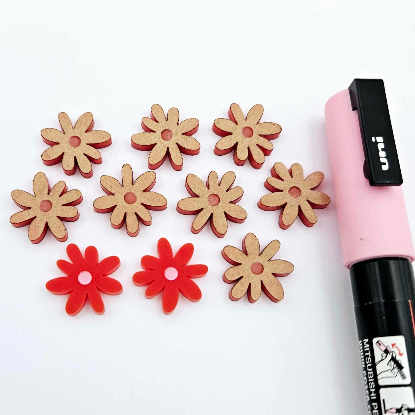 Red acrylic flower stud blanks showing paint filled light pink example and unpainted pieces with protective film, pictured with a light pink Posca paint pen
