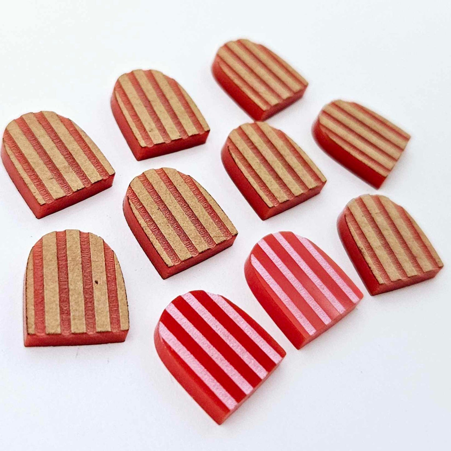 Red striped arch stud blanks with engraved stripes, one pair paint filled light pink and peeled, with additional unpainted pieces shown with protective film on