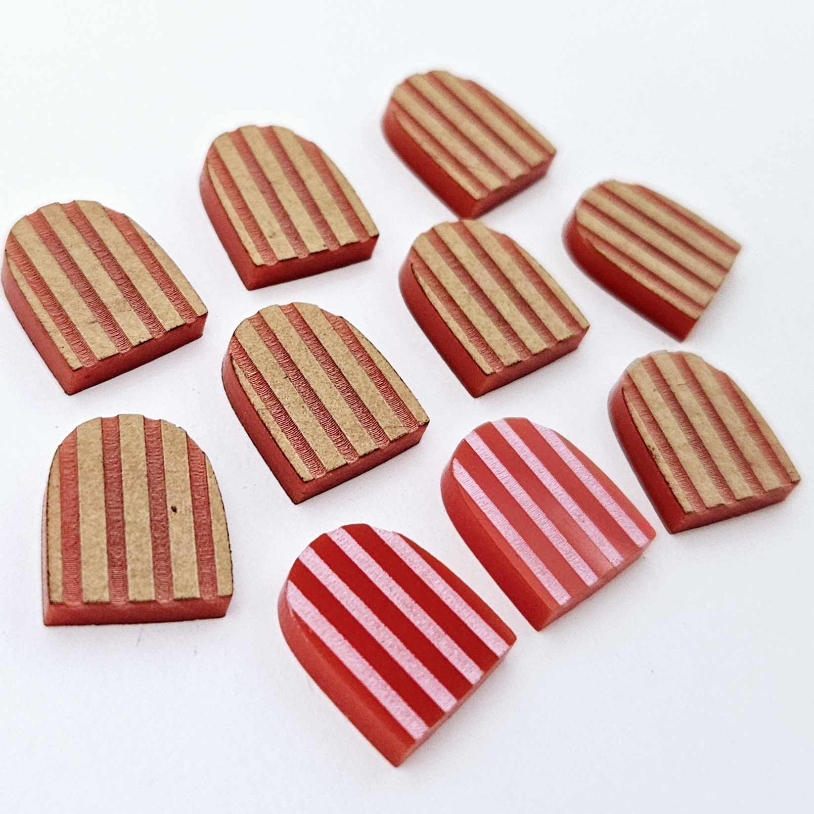 Red striped arch stud blanks with engraved stripes, one pair paint filled light pink and peeled, with additional unpainted pieces shown with protective film on