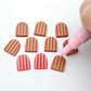 16mm red striped acrylic arch stud blanks showing paint filled example and unpainted pieces with protective film, pictured with a light pink Posca paint pen