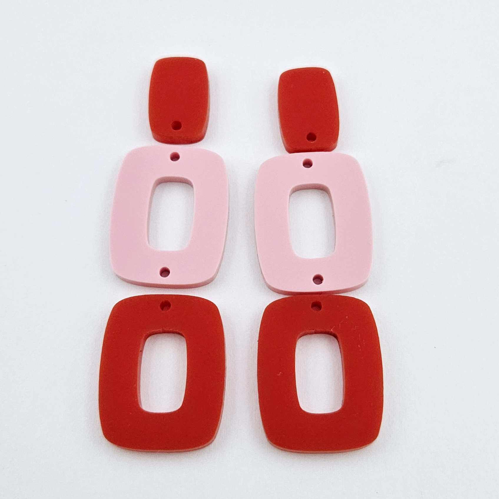 Layered rectangle dangle blanks in red and pastel pink, one pair shown unassembled laying flat with rectangle topper and two hoop pieces
