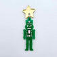 Assembled 40mm nutcracker Christmas dangle earrings in green acrylic with engraved detail paint filled with pink and white