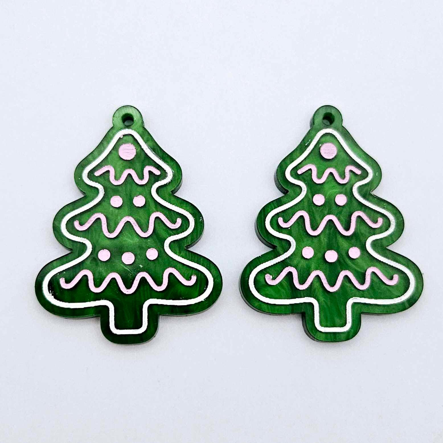 One pair of green marble cookie Christmas tree dangle blanks with engraved icing details paint filled in light pink and white, shown laying flat