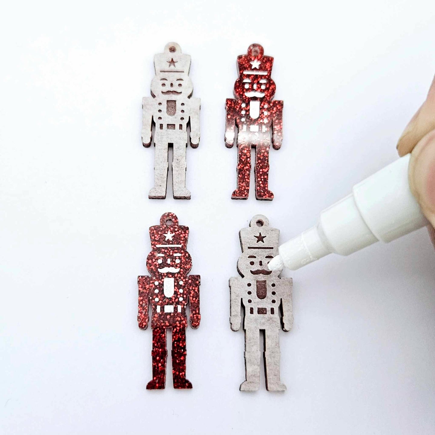 A pair of 40mm nutcracker Christmas dangle earring blanks in red glitter acrylic with engraved detail paint filled white with a pair not painted