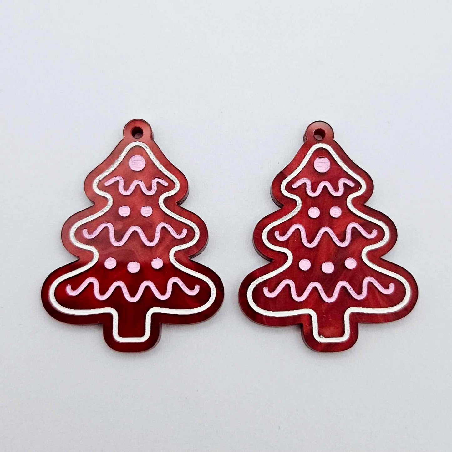One pair of deep red marble cookie Christmas tree dangle blanks with engraved icing details paint filled in light pink and white, shown laying flat