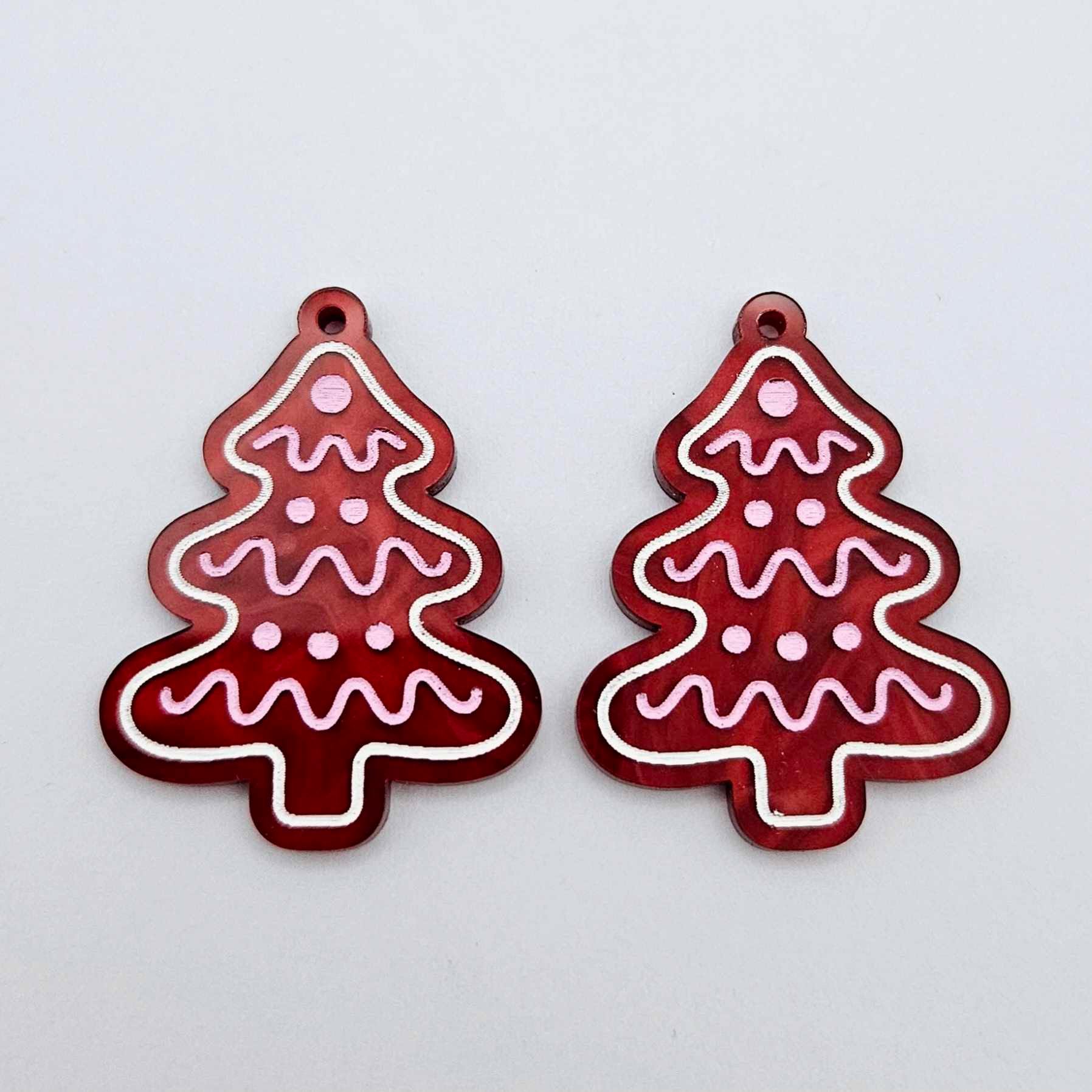 One pair of deep red marble cookie Christmas tree dangle blanks with engraved icing details paint filled in light pink and white, shown laying flat