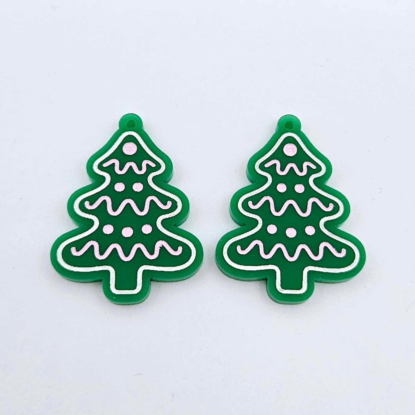 One pair of solid green cookie Christmas tree dangle blanks with engraved icing details paint filled in light pink and white, shown laying flat