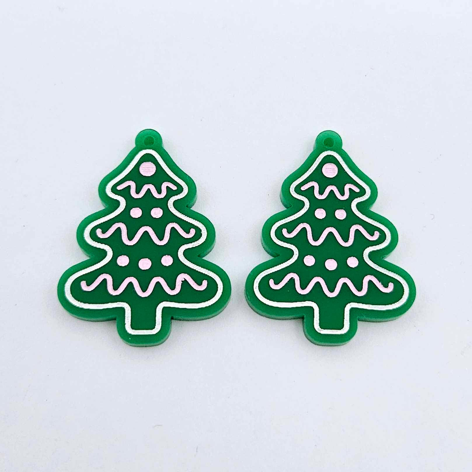 One pair of solid green cookie Christmas tree dangle blanks with engraved icing details paint filled in light pink and white, shown laying flat