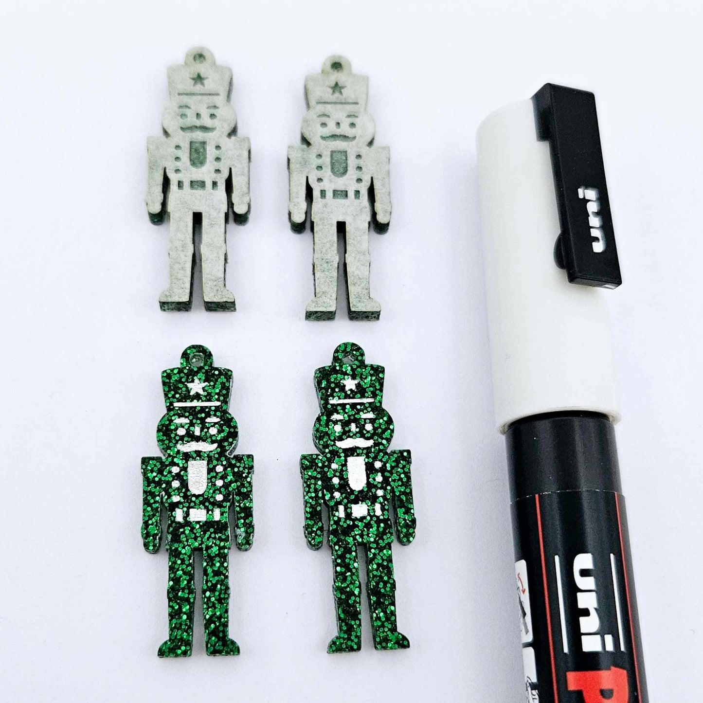 A pair of 40mm nutcracker Christmas dangle earring blanks in green glitter acrylic with engraved detail paint filled white with a paint not painted