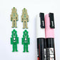 40mm nutcracker Christmas dangle blanks with engraved paint-fill details shown in  green acrylic with pink and white posca paint pens