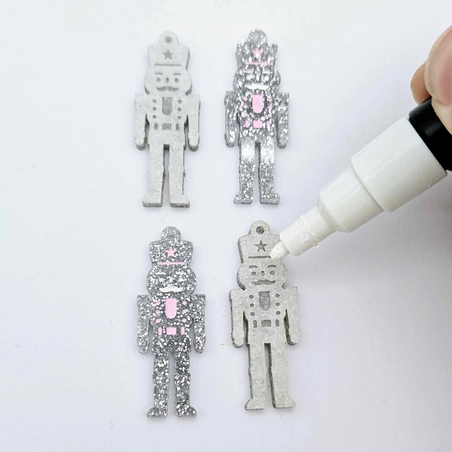 A pair of 40mm nutcracker Christmas dangle earring blanks in silver glitter acrylic with engraved detail paint filled white and pink and a pair not painted