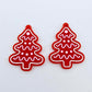 One pair of solid red cookie Christmas tree dangle earring blanks with engraved icing details paint filled in light pink and white, shown laying flat