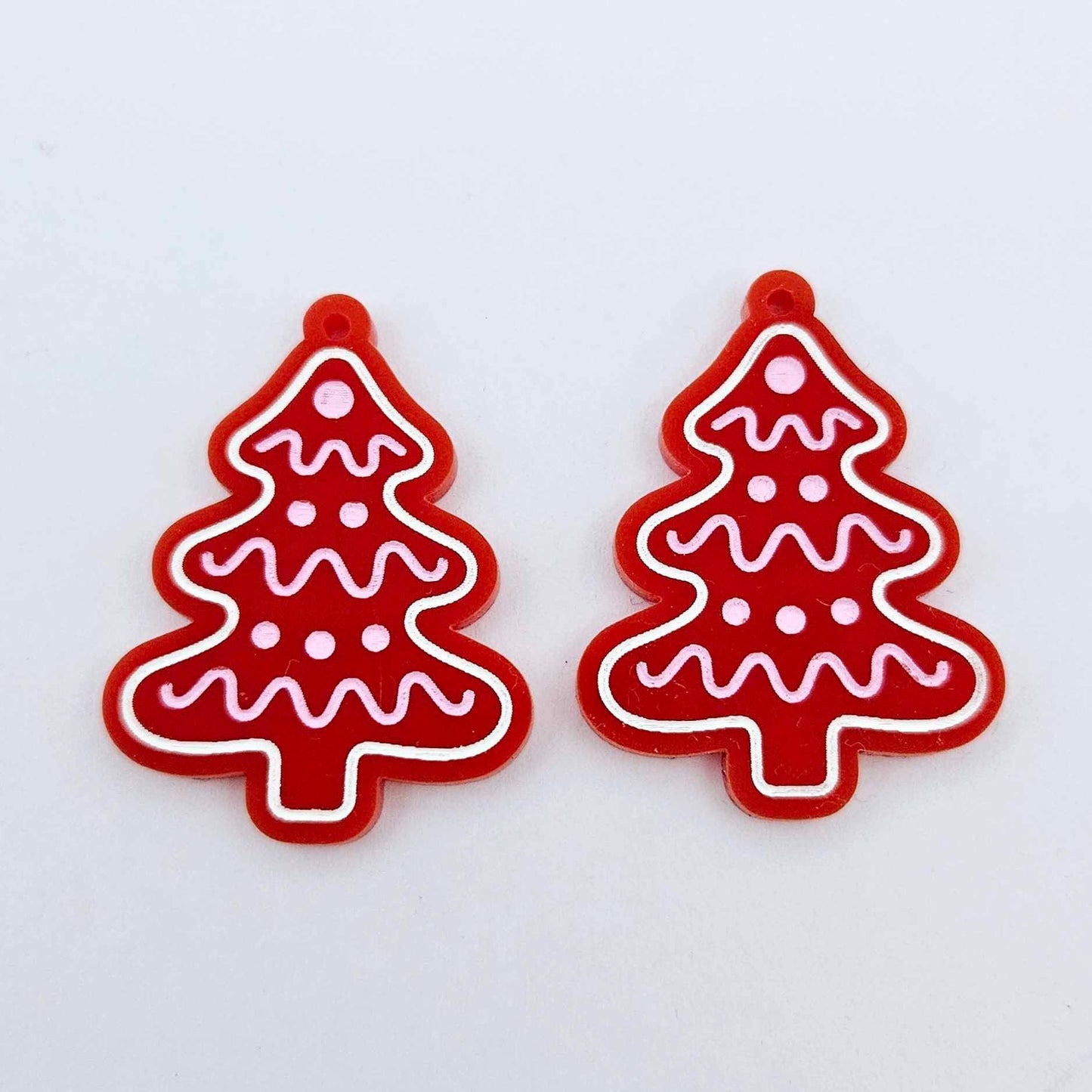 One pair of solid red cookie Christmas tree dangle earring blanks with engraved icing details paint filled in light pink and white, shown laying flat