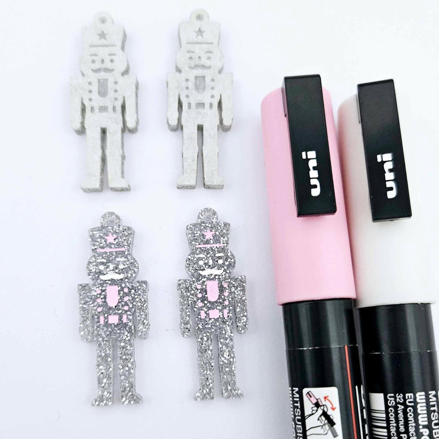 A pair of 40mm nutcracker Christmas dangle earring blanks in silver glitter acrylic with engraved detail paint filled white and pink and a pair not painted