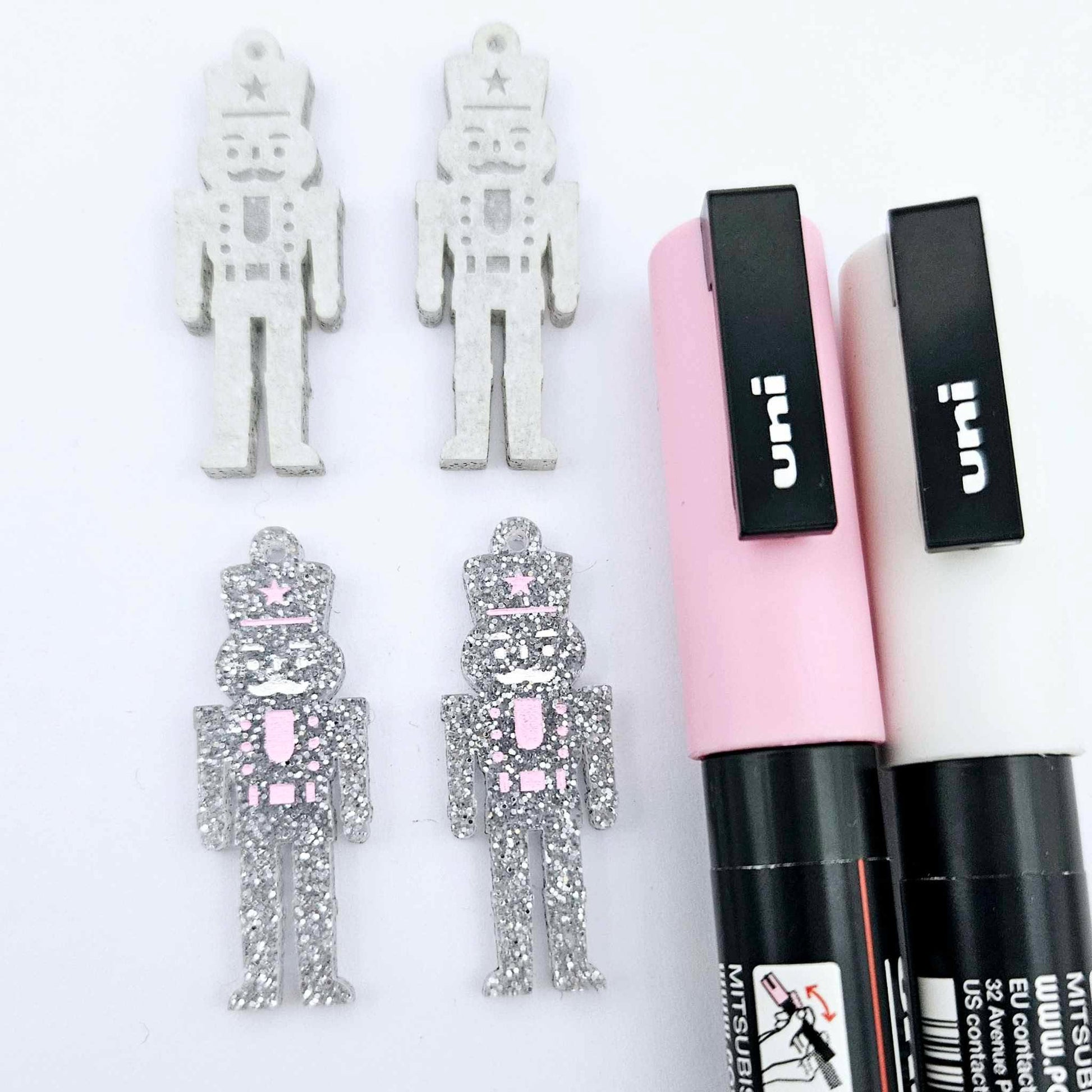 A pair of 40mm nutcracker Christmas dangle earring blanks in silver glitter acrylic with engraved detail paint filled white and pink and a pair not painted
