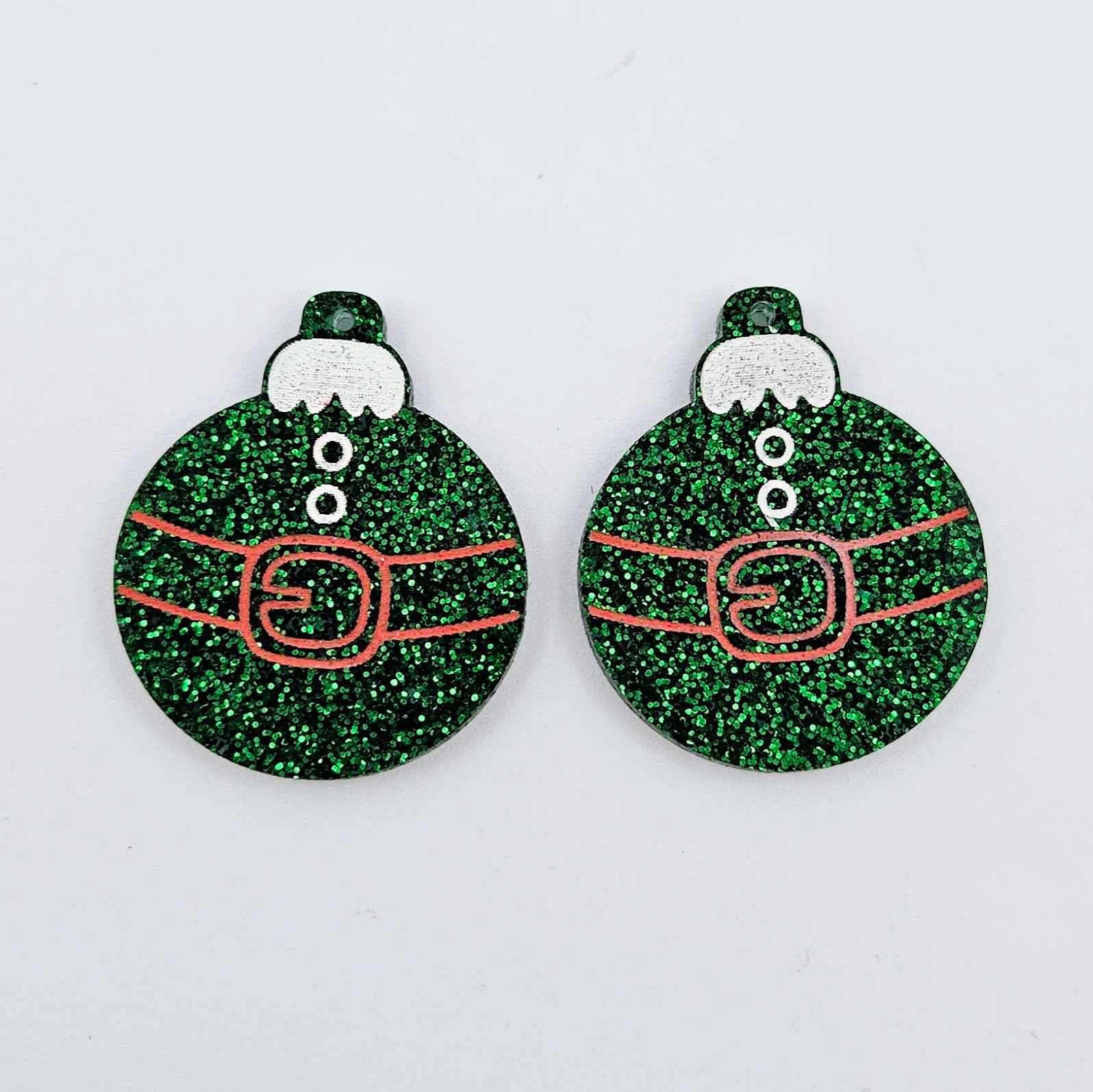 One pair of green glitter Santa bauble dangle blanks with engraved Santa belt and button details paint filled red and white, shown laying flat