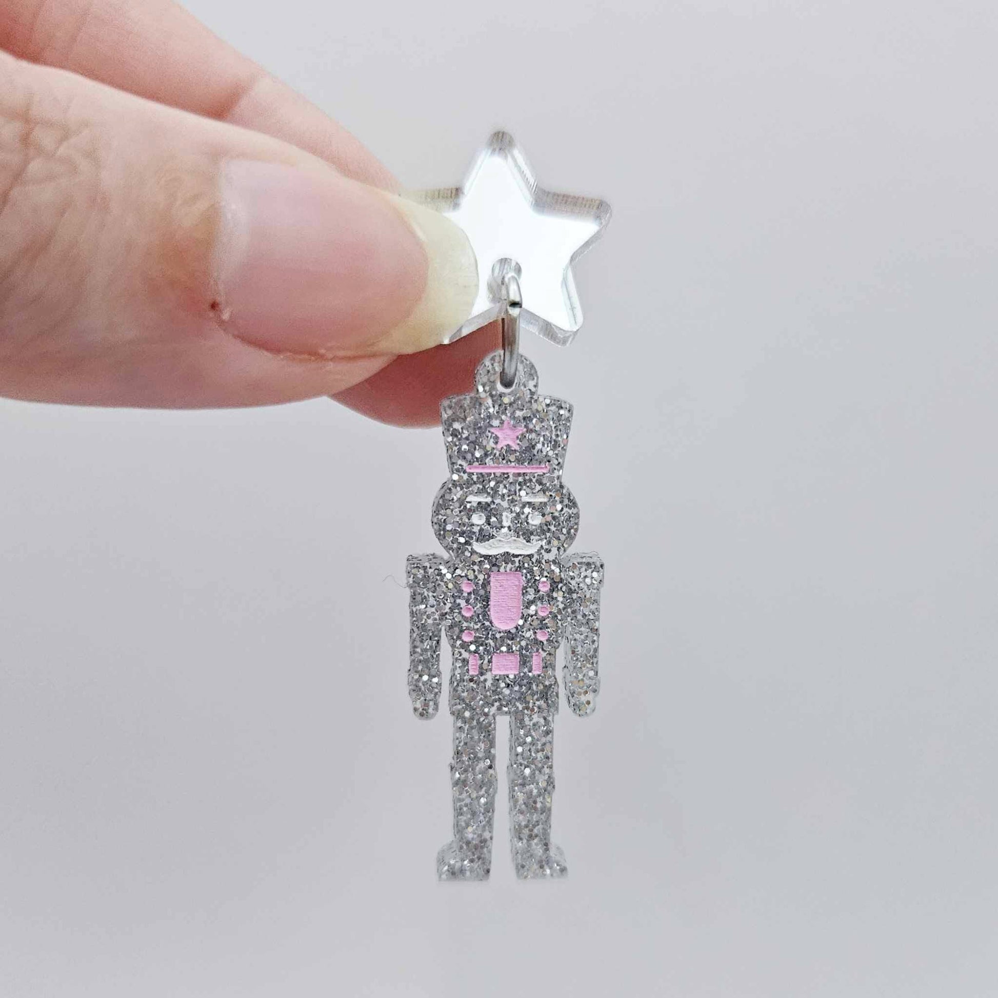 Assembled 40mm nutcracker Christmas dangle earrings in silver glitter acrylic with engraved detail paint filled white and pink