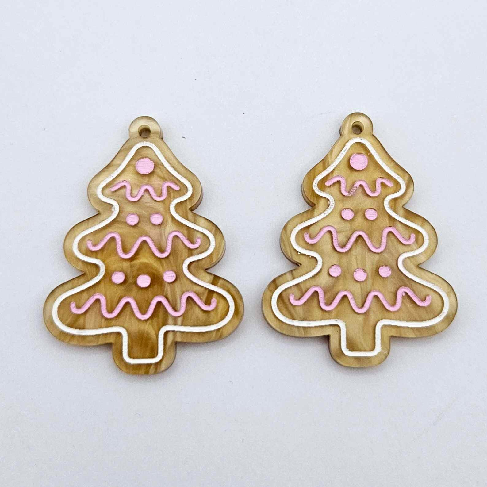 One pair of gold pearl marble cookie Christmas tree dangle earring blanks with engraved icing details paint filled in light pink and white, shown laying flat