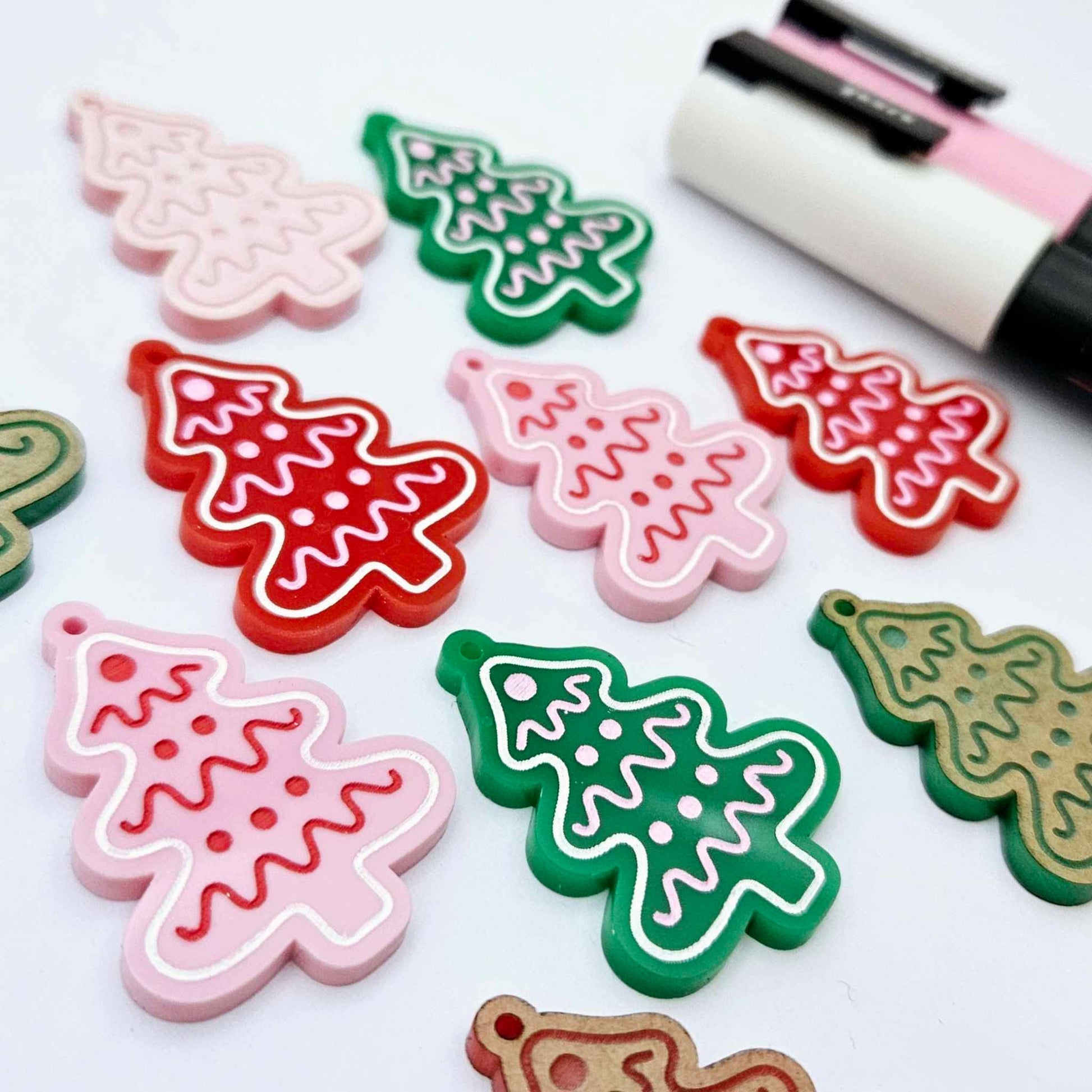 Cookie Christmas tree dangle earring blanks in solid red, solid green and pastel pink, showing a mix of paint-filled and unpainted pieces with Posca paint pens for customising the engraved icing details