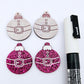 One pair of hot pink glitter Santa bauble dangle earring blanks paint filled white, alongside one unpainted pair with protective paper attached, pictured with a Posca paint pen