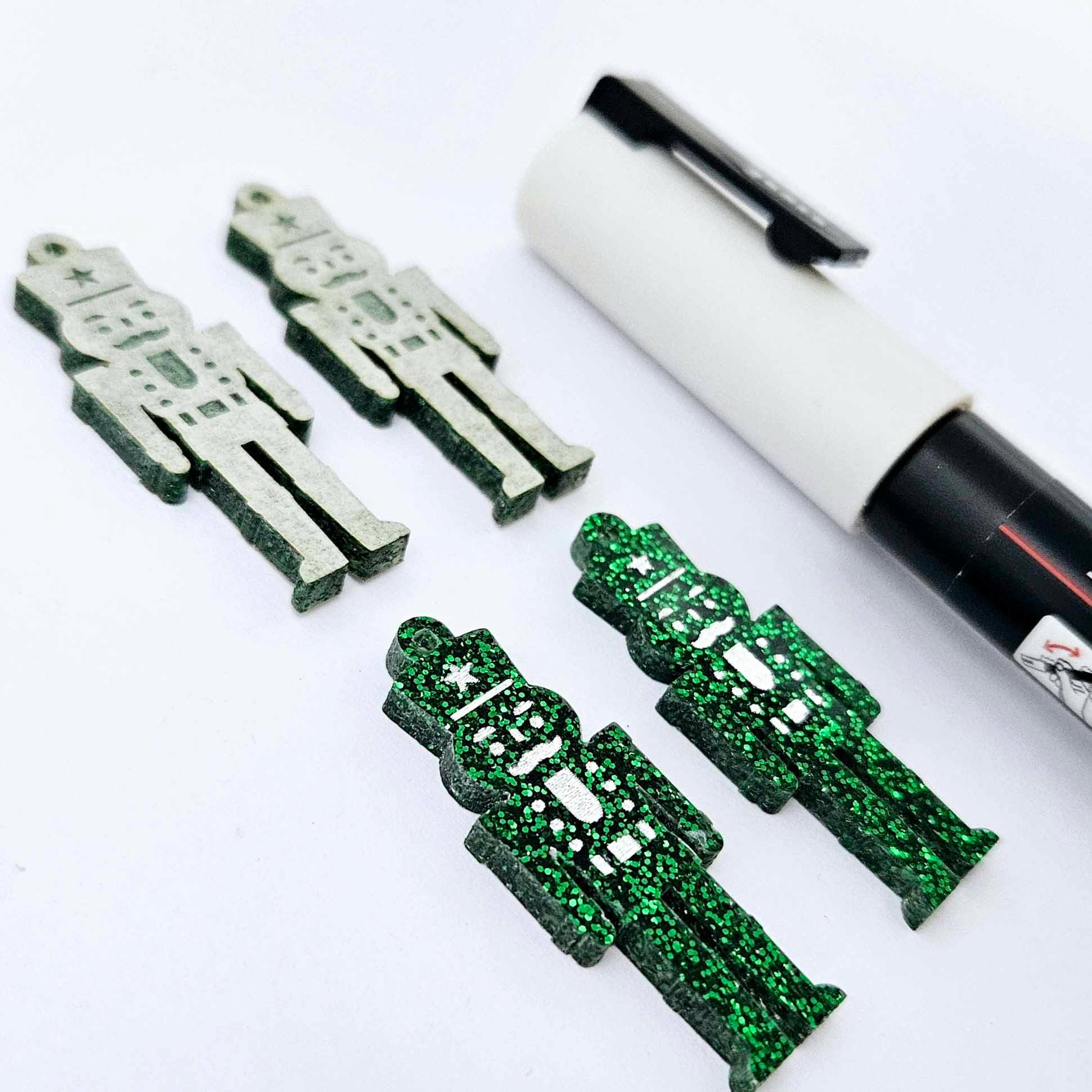 A pair of 40mm nutcracker Christmas dangle earring blanks in green glitter acrylic with engraved detail paint filled white with a paint not painted