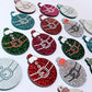 Red, green, teal, silver and hot pink glitter Santa bauble dangle blanks paint filled, alongside unpainted pieces with protective paper attached
