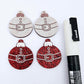 One pair of red glitter Santa bauble dangle blanks paint filled white, alongside one unpainted pair with protective paper attached, pictured with Posca paint pens