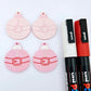 One pair of pastel pink Santa bauble dangle blanks paint filled in white and red, alongside one unpainted pair with protective paper attached, pictured with Posca paint pens