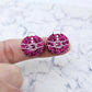 One pair of hot pink glitter Santa bauble stud earring blanks with engraved Santa belt and button details paint filled white, shown on a finger for size reference