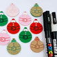 One paint-filled pair each of solid red, solid green and pastel pink Santa bauble dangle blanks, with additional unpainted blanks still covered with protective paper scattered around, showing the paint-fill possibilities.