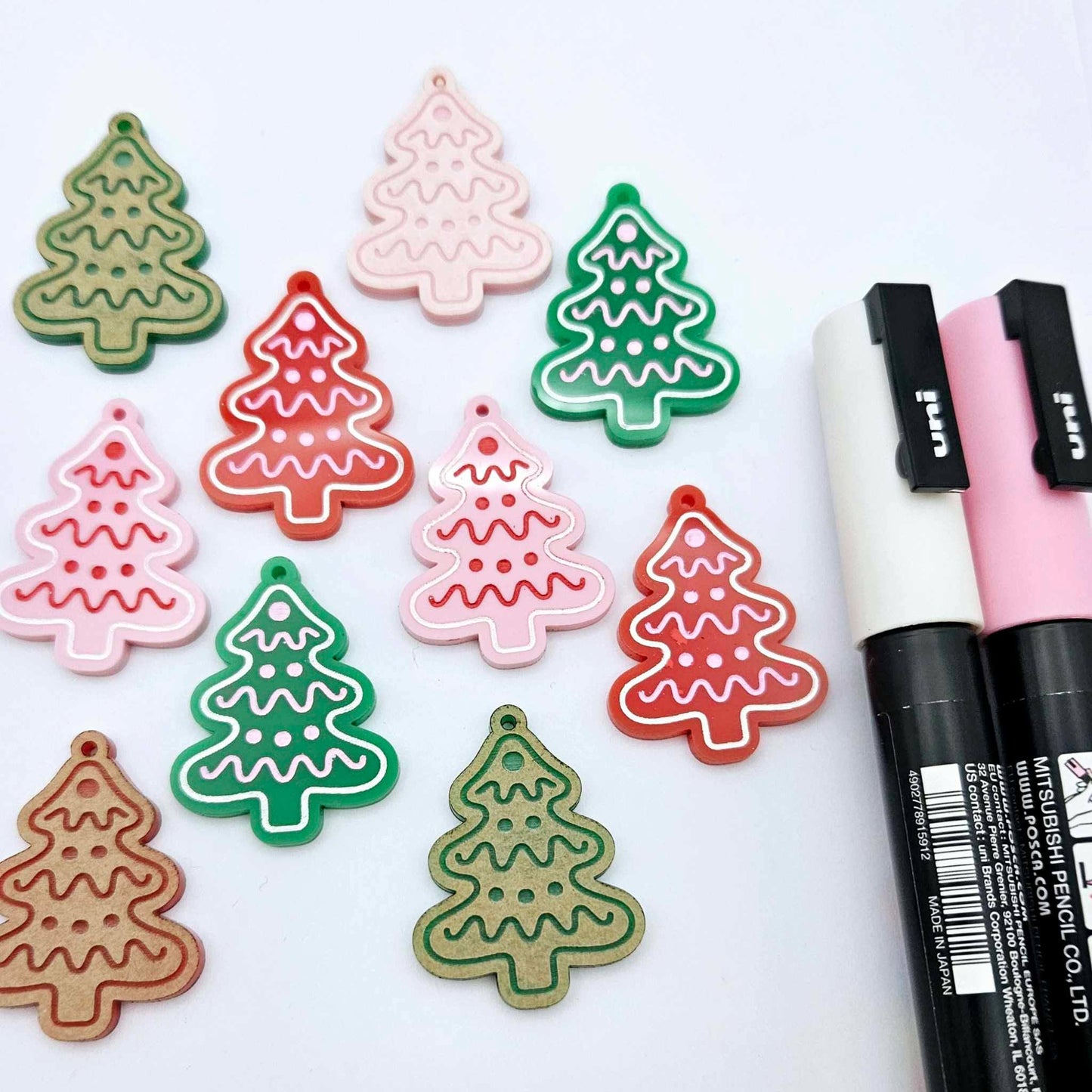 Cookie Christmas tree dangle earring blanks in solid red, solid green and pastel pink, showing a mix of paint-filled and unpainted pieces with Posca paint pens for customising the engraved icing details