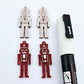A pair of 40mm nutcracker Christmas dangle earring blanks in red glitter acrylic with engraved detail paint filled white with a pair not painted