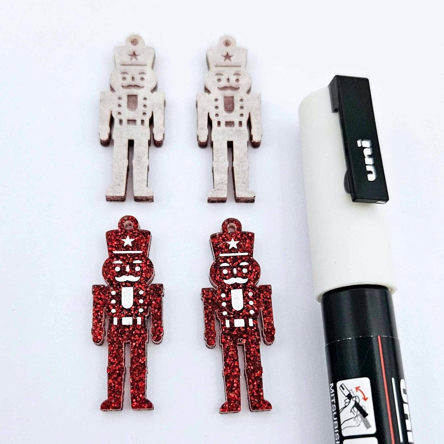 A pair of 40mm nutcracker Christmas dangle earring blanks in red glitter acrylic with engraved detail paint filled white with a pair not painted