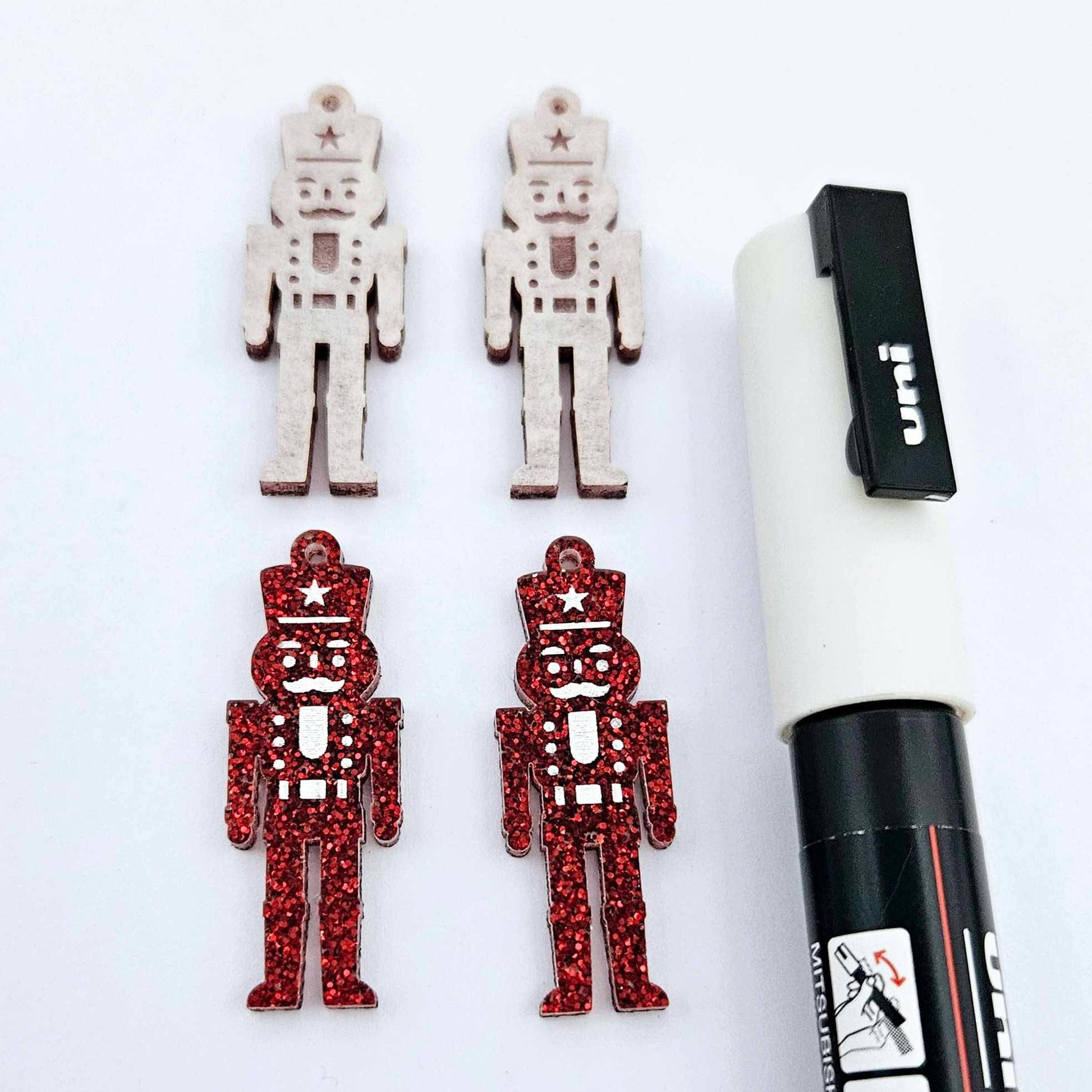 A pair of 40mm nutcracker Christmas dangle earring blanks in red glitter acrylic with engraved detail paint filled white with a pair not painted