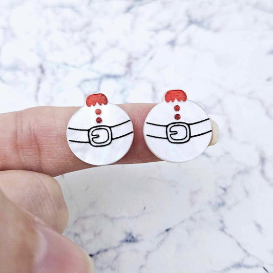 One pair of white marble Santa bauble stud earring blanks with engraved Santa belt and button details paint filled red and black, shown on a finger for size reference