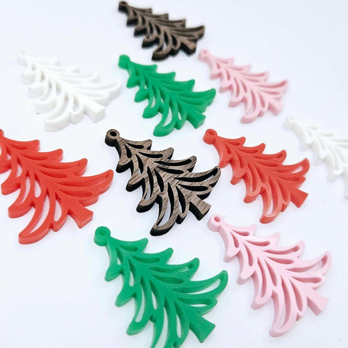 A mixture of solid green, solid red, white, pastel pink and walnut veneer 35mm Cascade Christmas Tree dangle earring blanks laying flat on a white background