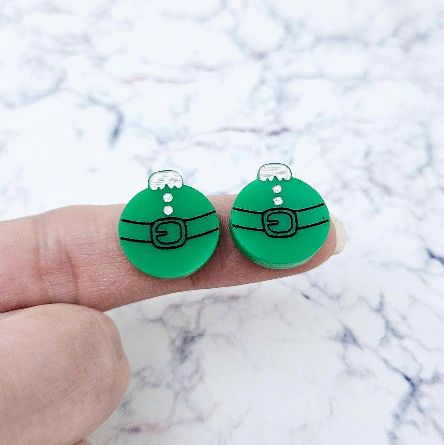 One pair of solid green Santa bauble stud earring blanks with engraved Santa belt and button details paint filled black and white, shown on a finger for size reference