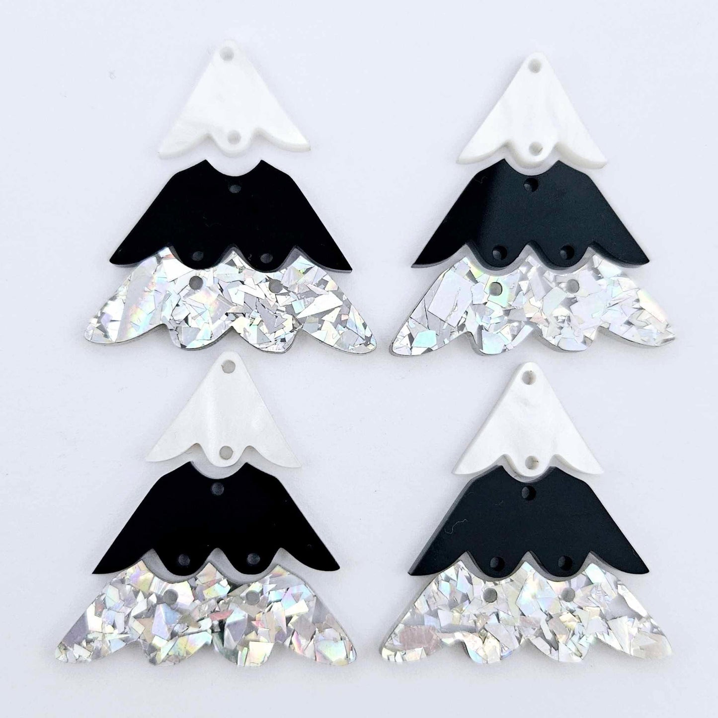 Two pairs of 40mm three piece Christmas Tree dangle earring blanks in holographic silver glitter, black and white marble acrylic laying flat on a white background