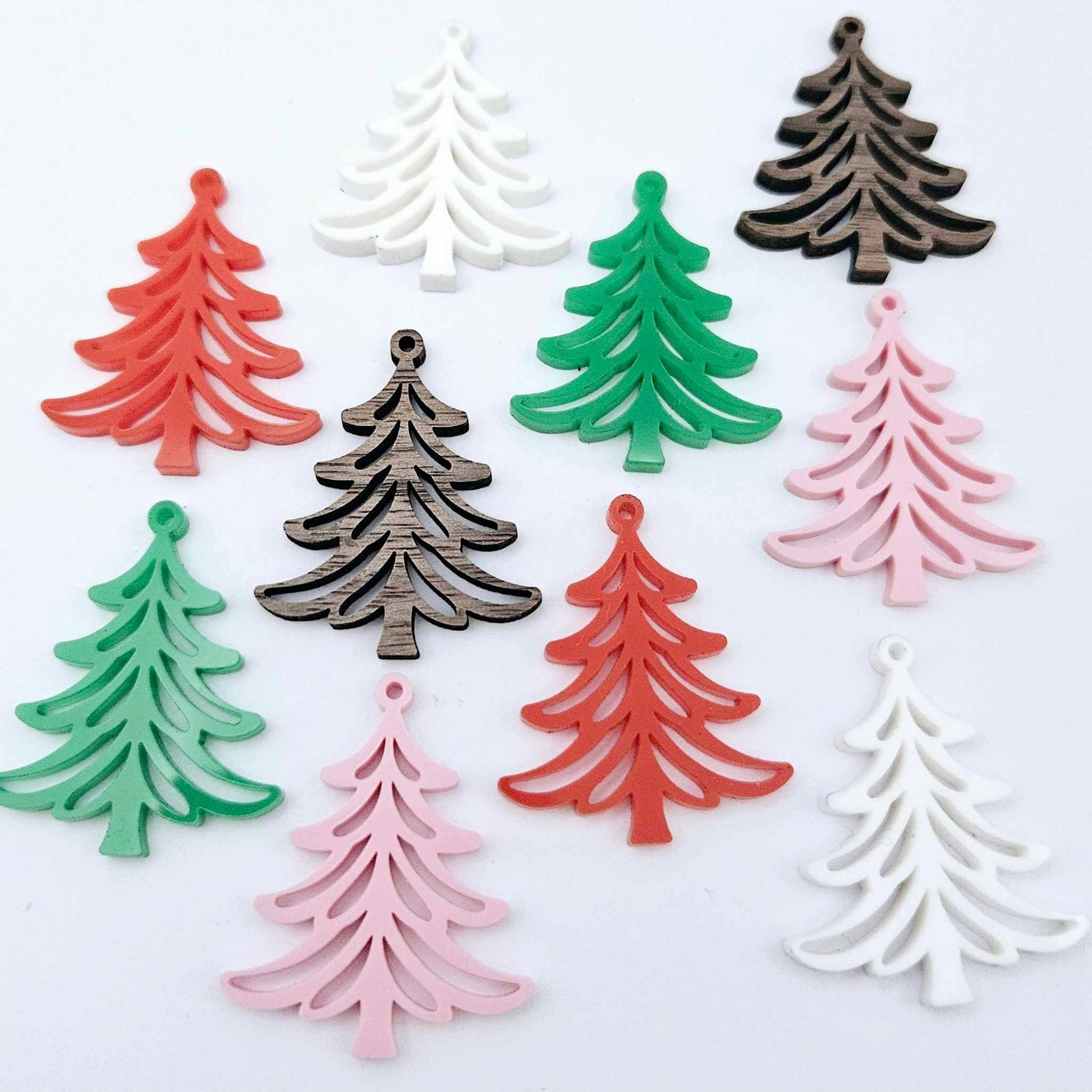 A mixture of solid green, solid red, white, pastel pink and walnut veneer 35mm Cascade Christmas Tree dangle earring blanks laying flat on a white background